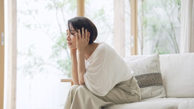 Distraught woman covering ears with hands, eyes closed, sitting on couch