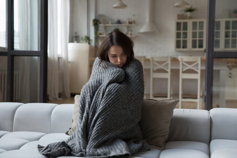 Young, upset woman curled up in blanket on couch