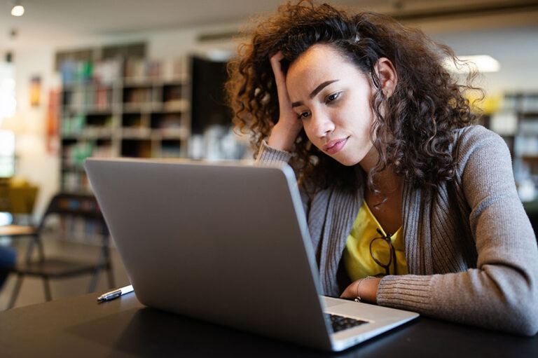 Woman staring at laptop, hand on head, looking bummed out