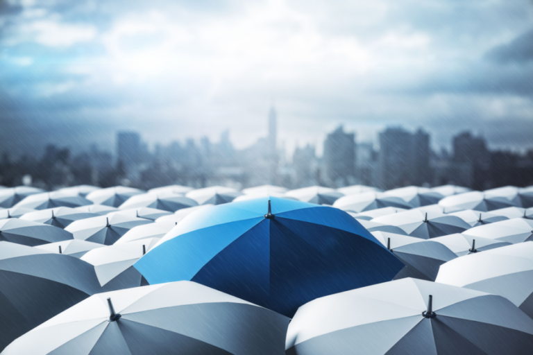 An image of a blue umbrella in a sea of gray umbrellas to indicate 