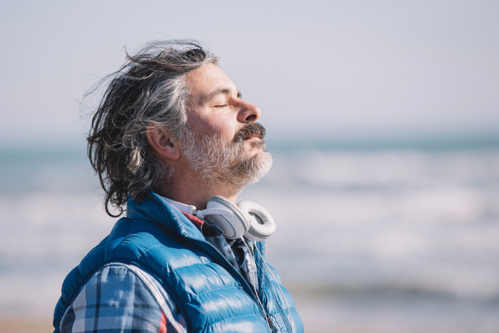 Man in vest taking a deep breath at beach after learning how to calm down anxiety