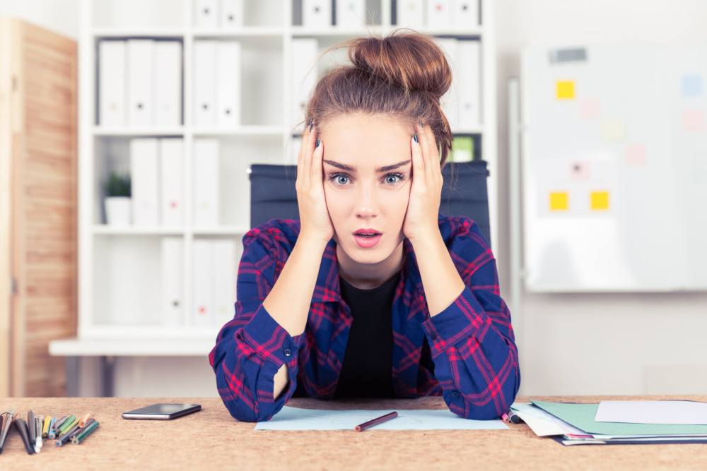 Woman at desk wearing blue and red plaid blouse holding her head in exasperation over false memory OCD