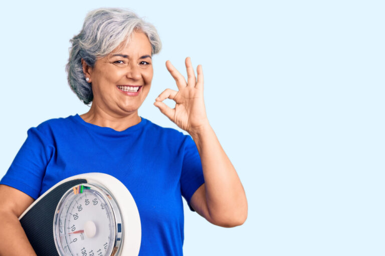 Woman holding scale giving the okay sign because she used weight loss injections and lost pounds