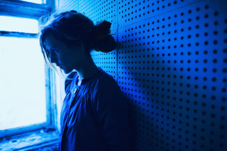 Woman with head down looking out window in all blue wondering what causes OCD to get worse