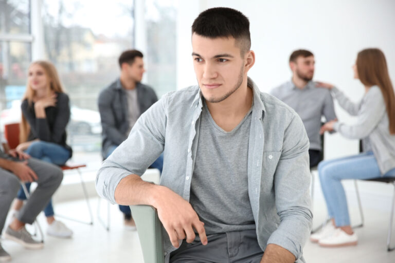 Young man isolated from others in background wondering how to overcome social anxiety.